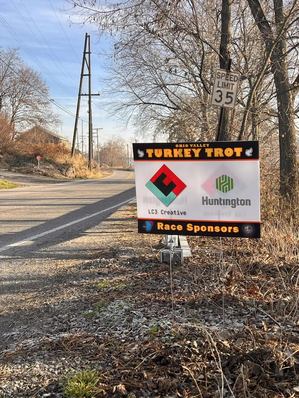 An Ohio Valley Turkey Trot race sponsors sign beside a country road, showing the LC3 Creative and Huntington logos.